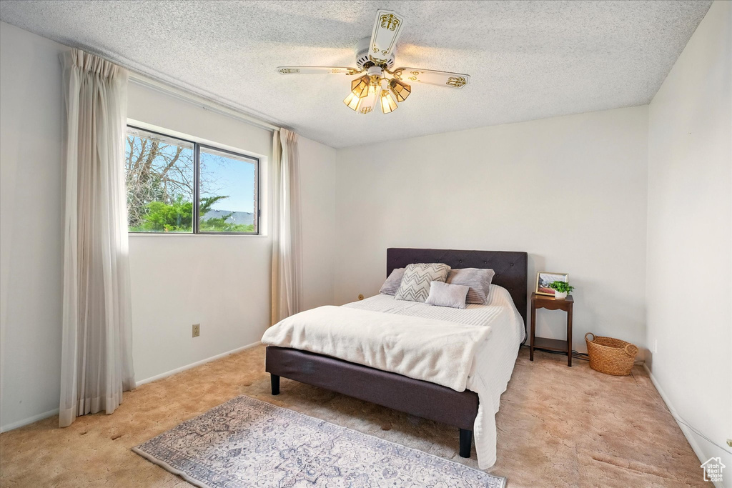 Bedroom featuring ceiling fan, light carpet, a textured ceiling, and baseboards