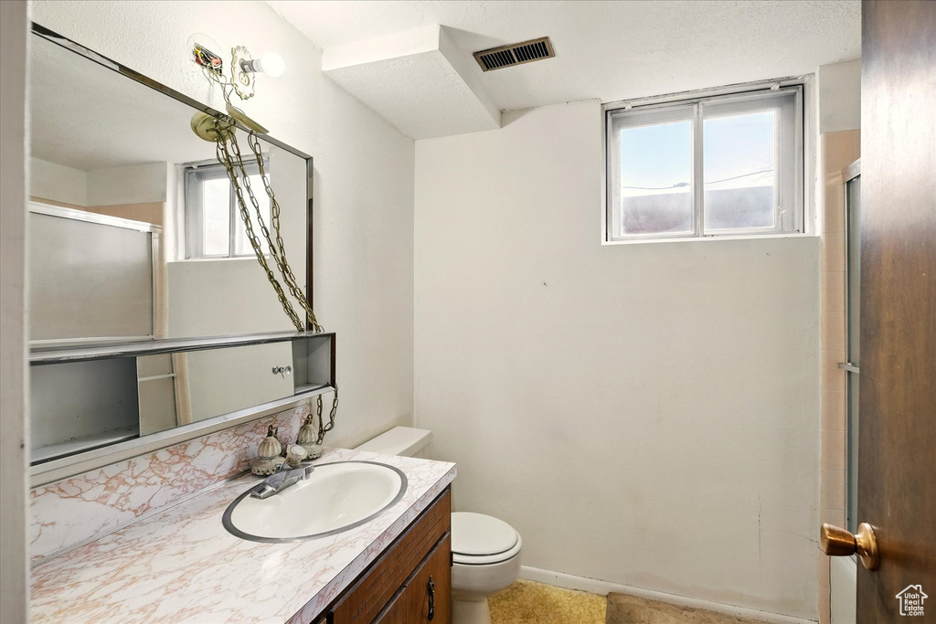 Bathroom with toilet, a shower with door, vanity, and visible vents