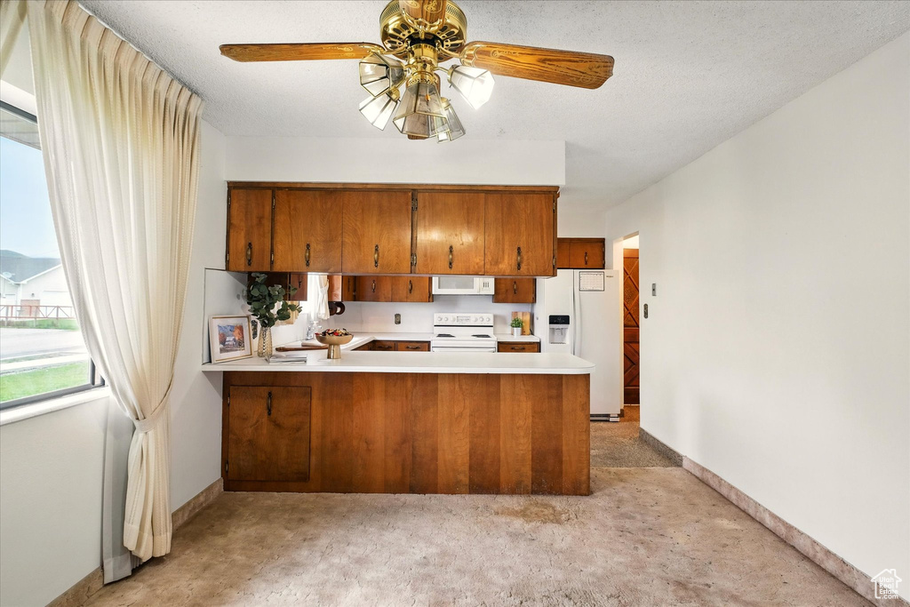 Kitchen featuring a peninsula, brown cabinets, ceiling fan, white appliances, and light countertops