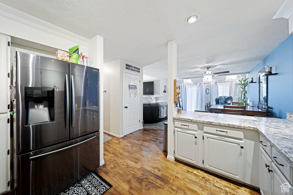 Kitchen featuring stainless steel fridge with ice dispenser, ceiling fan, light wood finished floors, white cabinetry, and light stone countertops