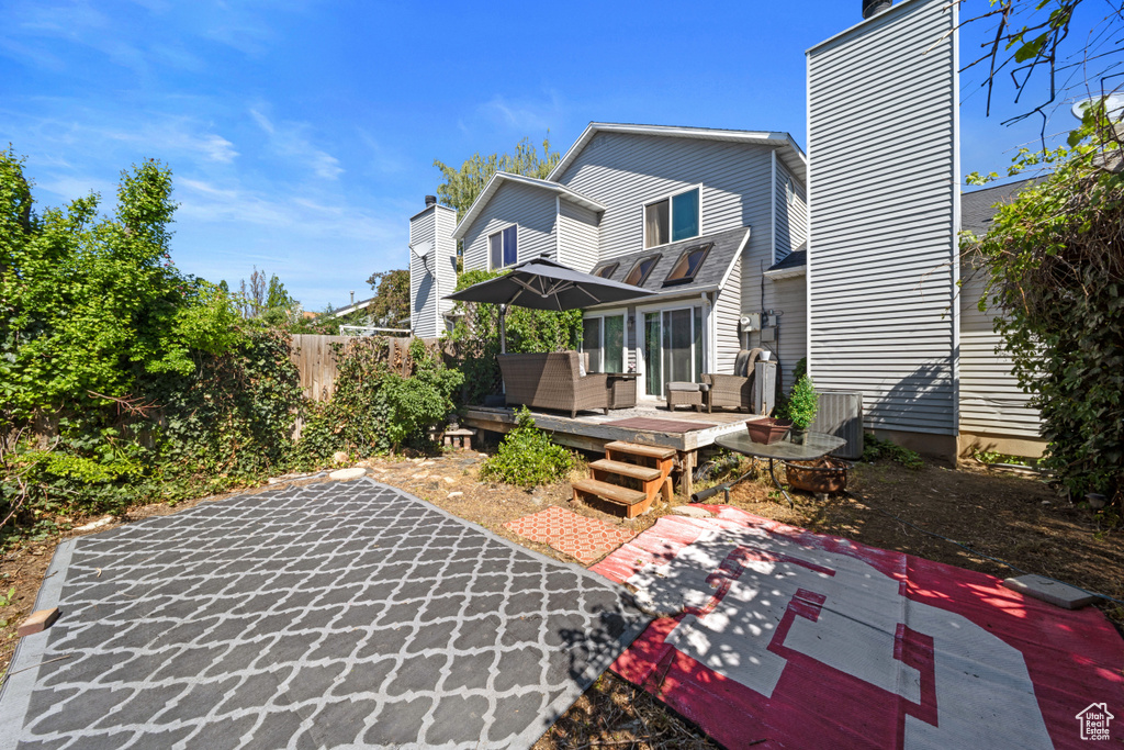 Rear view of property featuring a wooden deck, a patio, a chimney, and fence