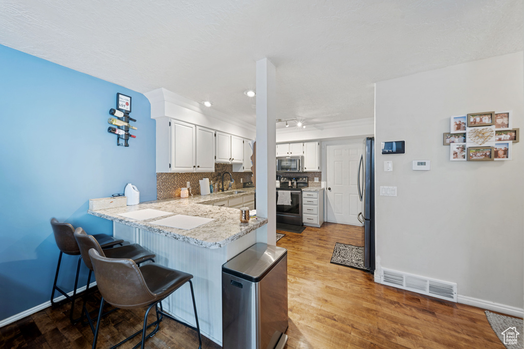 Kitchen featuring stainless steel appliances, a peninsula, a kitchen bar, decorative backsplash, and a sink