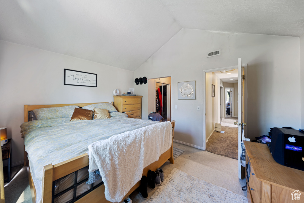 Bedroom with light colored carpet, vaulted ceiling, a walk in closet, a closet, and baseboards