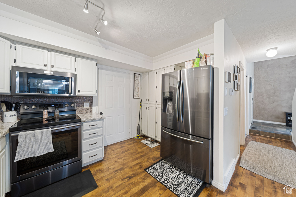 Kitchen with appliances with stainless steel finishes, a textured ceiling, dark wood-style flooring, white cabinetry, and light stone counters