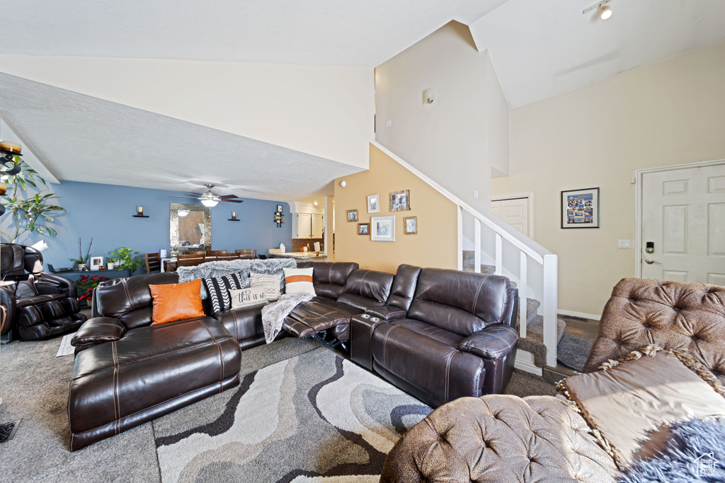 Carpeted living room with stairway, high vaulted ceiling, and a ceiling fan