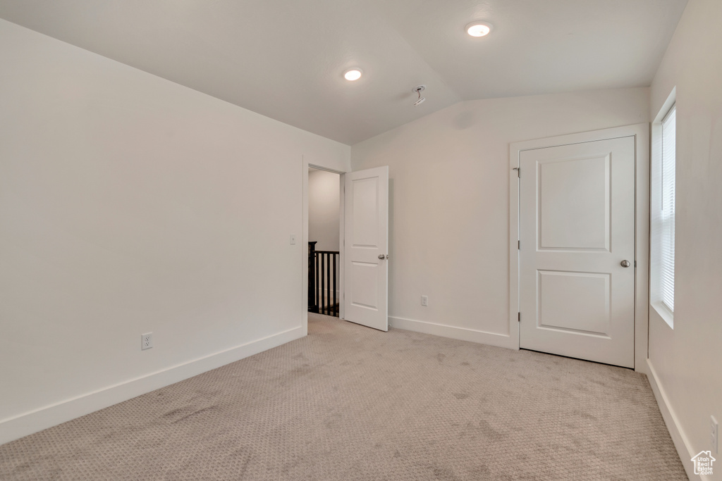 Unfurnished bedroom with vaulted ceiling, light carpet, and baseboards