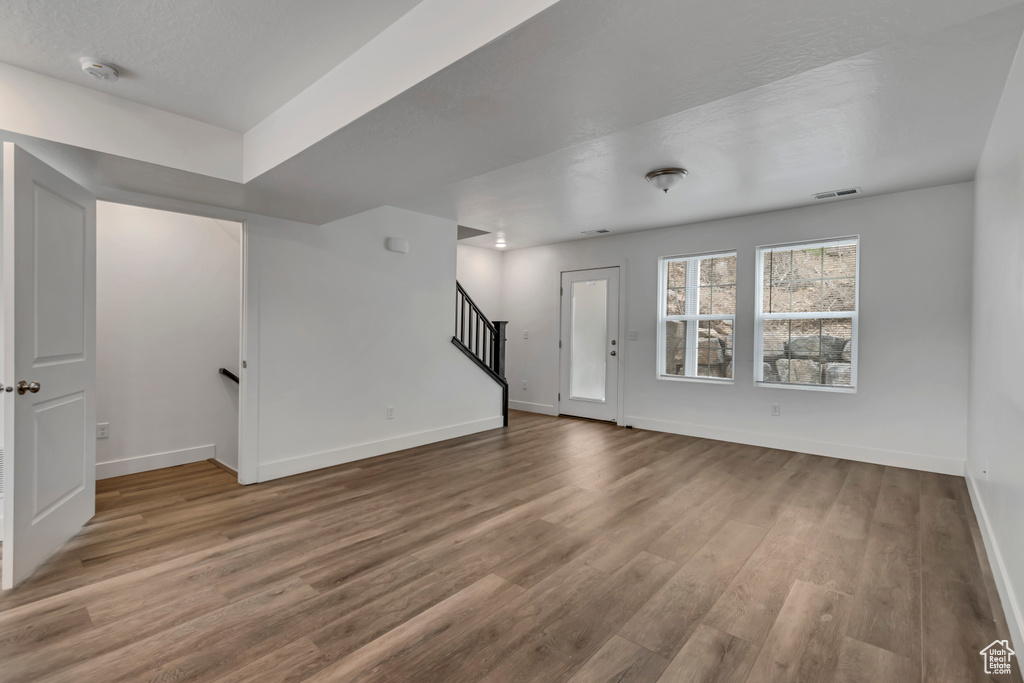 Unfurnished living room featuring stairway, baseboards, visible vents, and wood finished floors