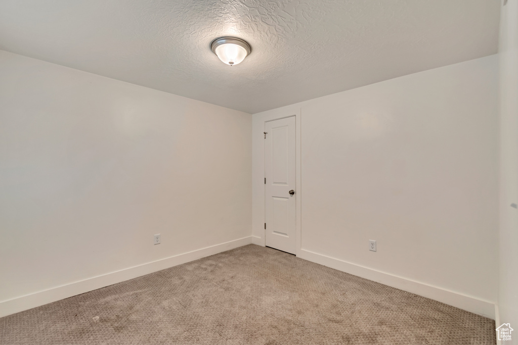 Empty room featuring baseboards, a textured ceiling, and light colored carpet