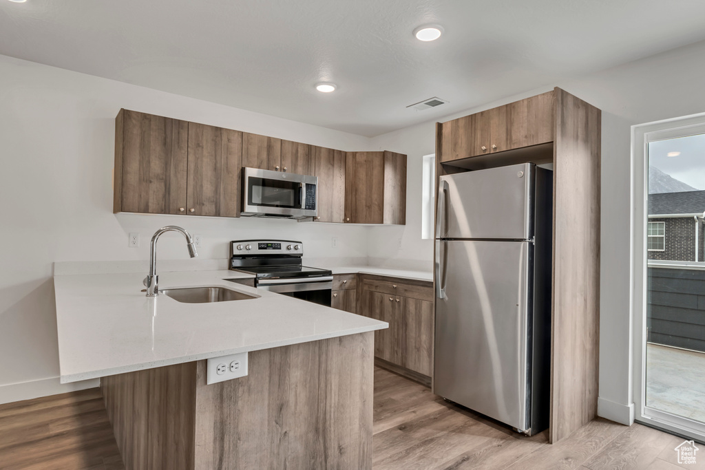 Kitchen featuring a sink, a peninsula, appliances with stainless steel finishes, light countertops, and light wood-style floors