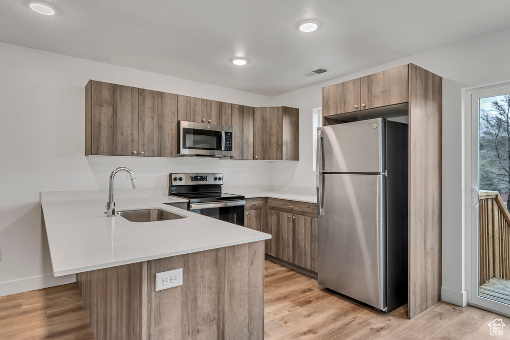 Kitchen with a sink, a peninsula, light wood-style flooring, light countertops, and appliances with stainless steel finishes