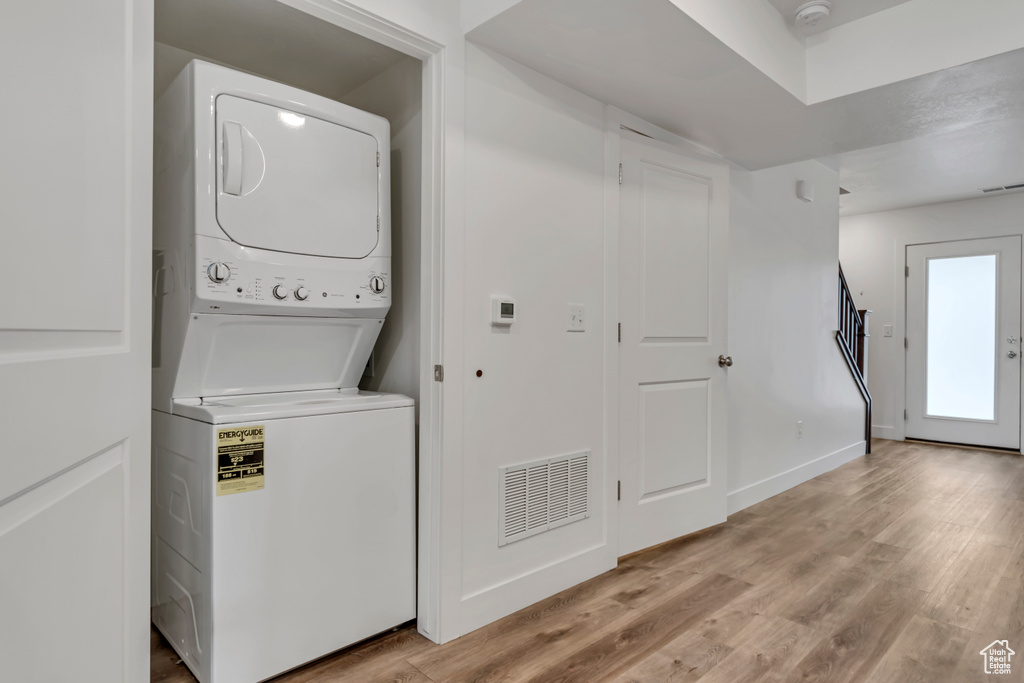 Washroom featuring baseboards, light wood finished floors, visible vents, laundry area, and stacked washer / drying machine
