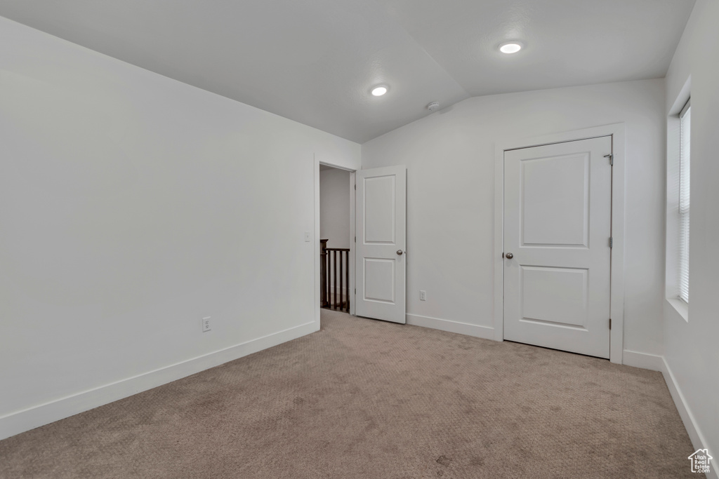 Unfurnished bedroom with lofted ceiling, baseboards, and light colored carpet