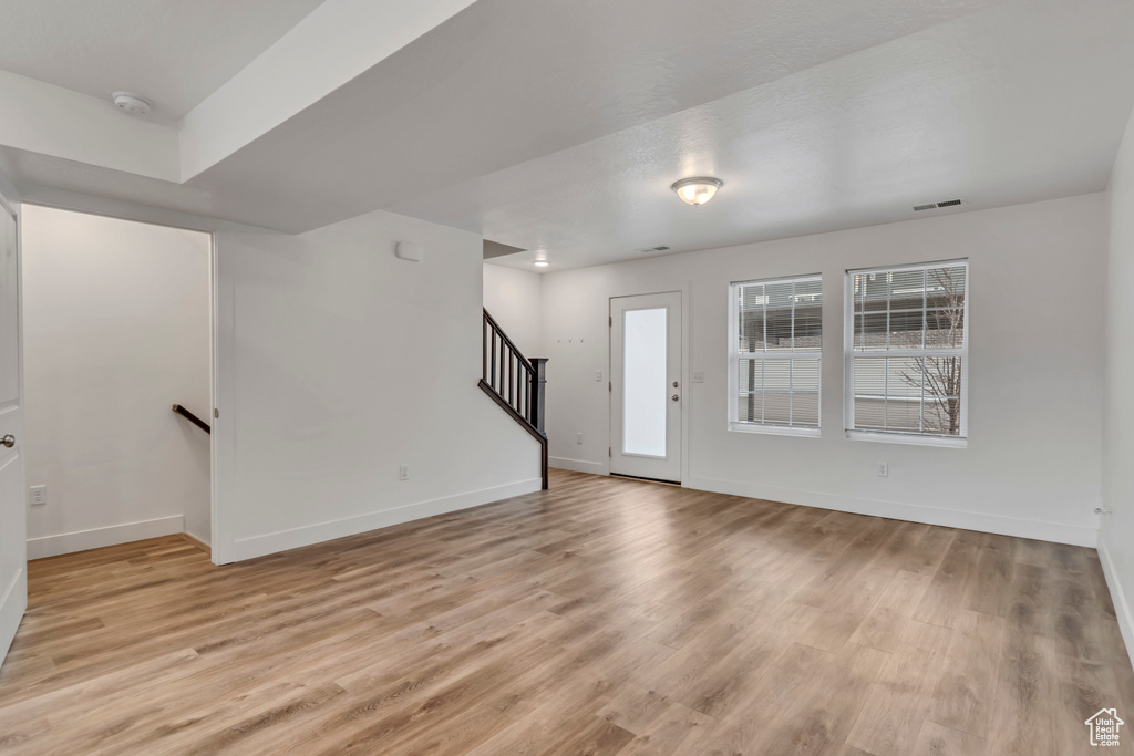 Unfurnished living room with visible vents, baseboards, light wood-style flooring, and stairs
