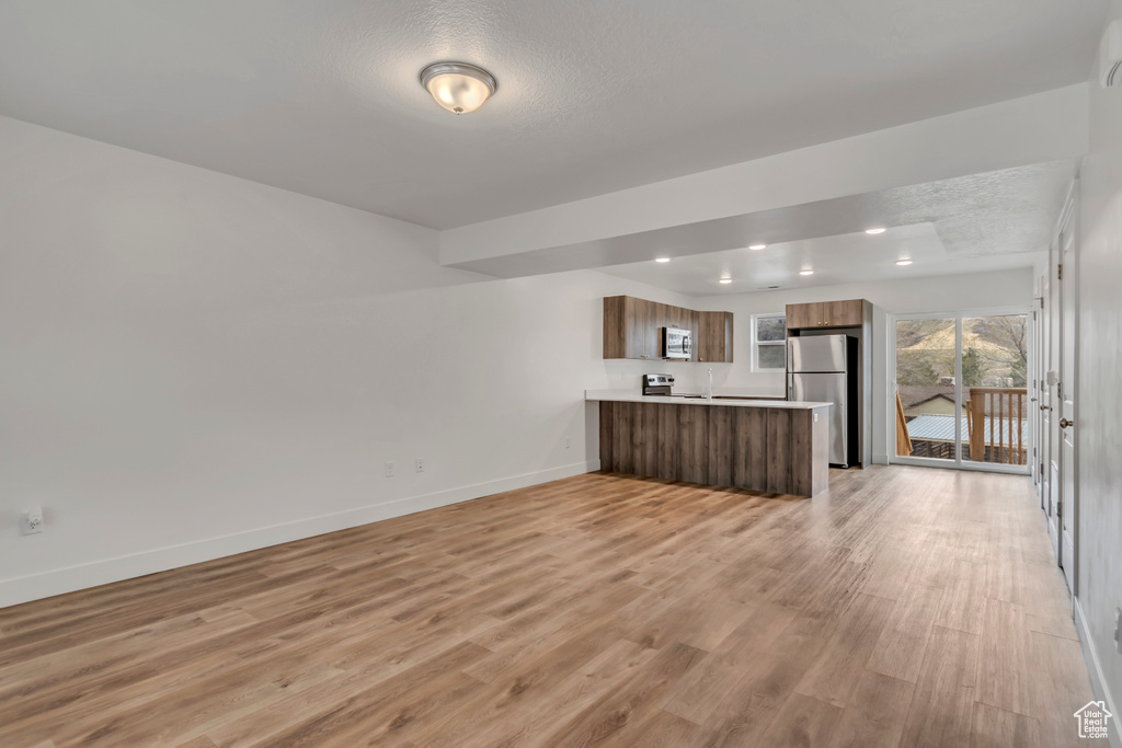 Kitchen with appliances with stainless steel finishes, open floor plan, a peninsula, light countertops, and light wood-type flooring