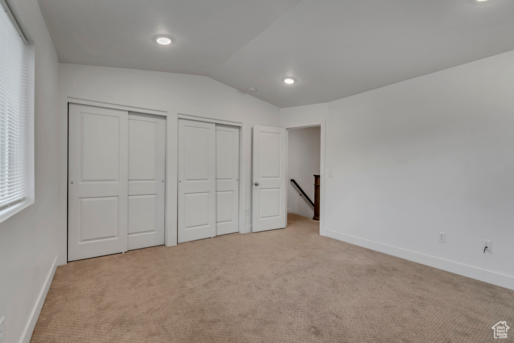 Unfurnished bedroom featuring carpet flooring, baseboards, lofted ceiling, and multiple closets