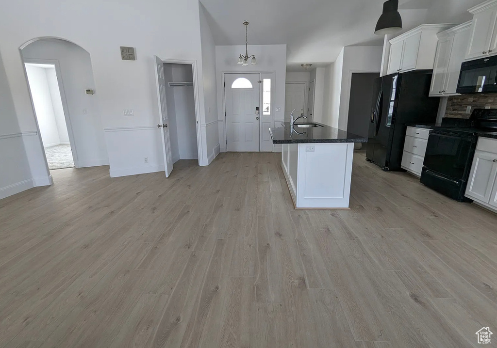 Kitchen with light wood finished floors, arched walkways, black appliances, and white cabinets