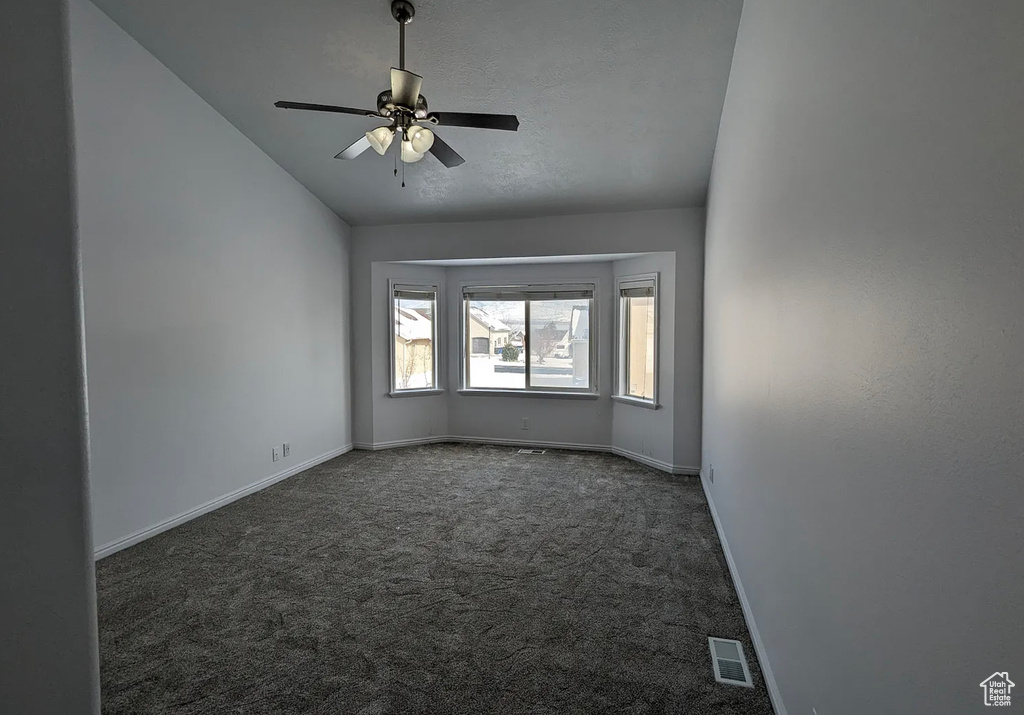 Carpeted spare room with vaulted ceiling, baseboards, a ceiling fan, and visible vents