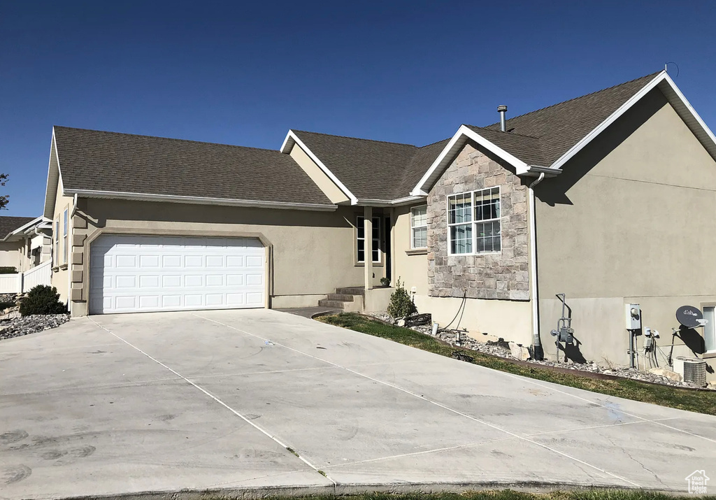 Single story home featuring stone siding, an attached garage, central AC, stucco siding, and driveway