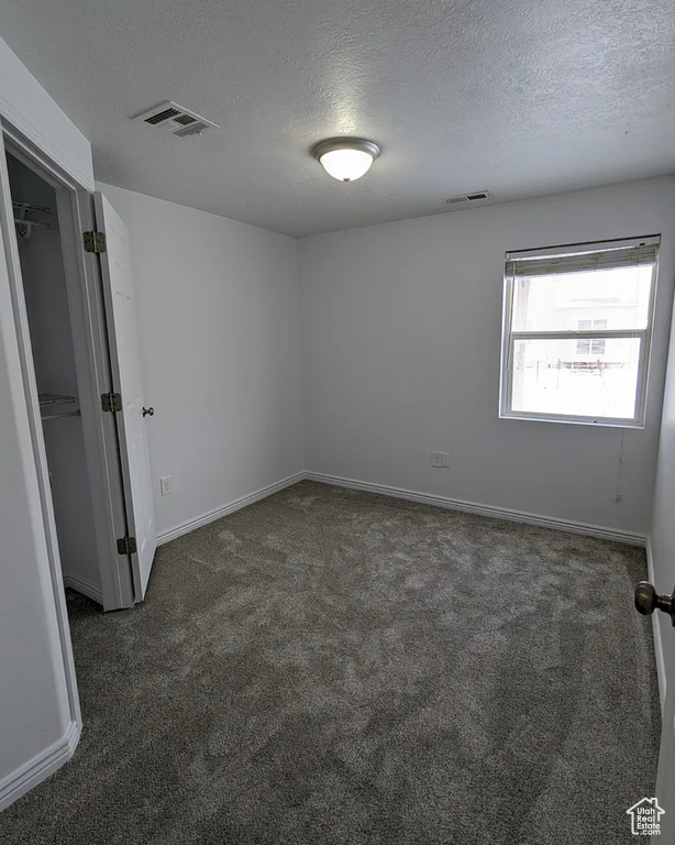 Carpeted empty room with a textured ceiling, visible vents, and baseboards
