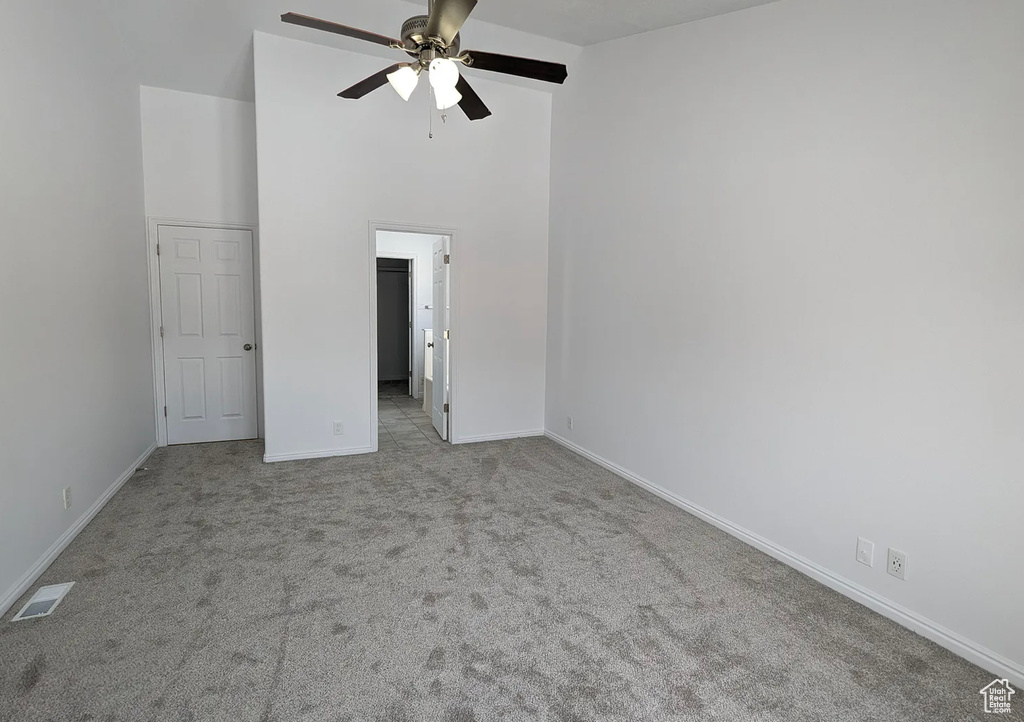 Unfurnished bedroom with carpet, visible vents, a walk in closet, a high ceiling, and baseboards