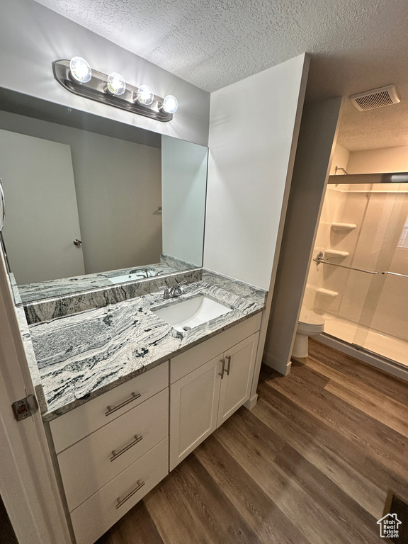 Bathroom with a stall shower, a textured ceiling, visible vents, vanity, and wood finished floors