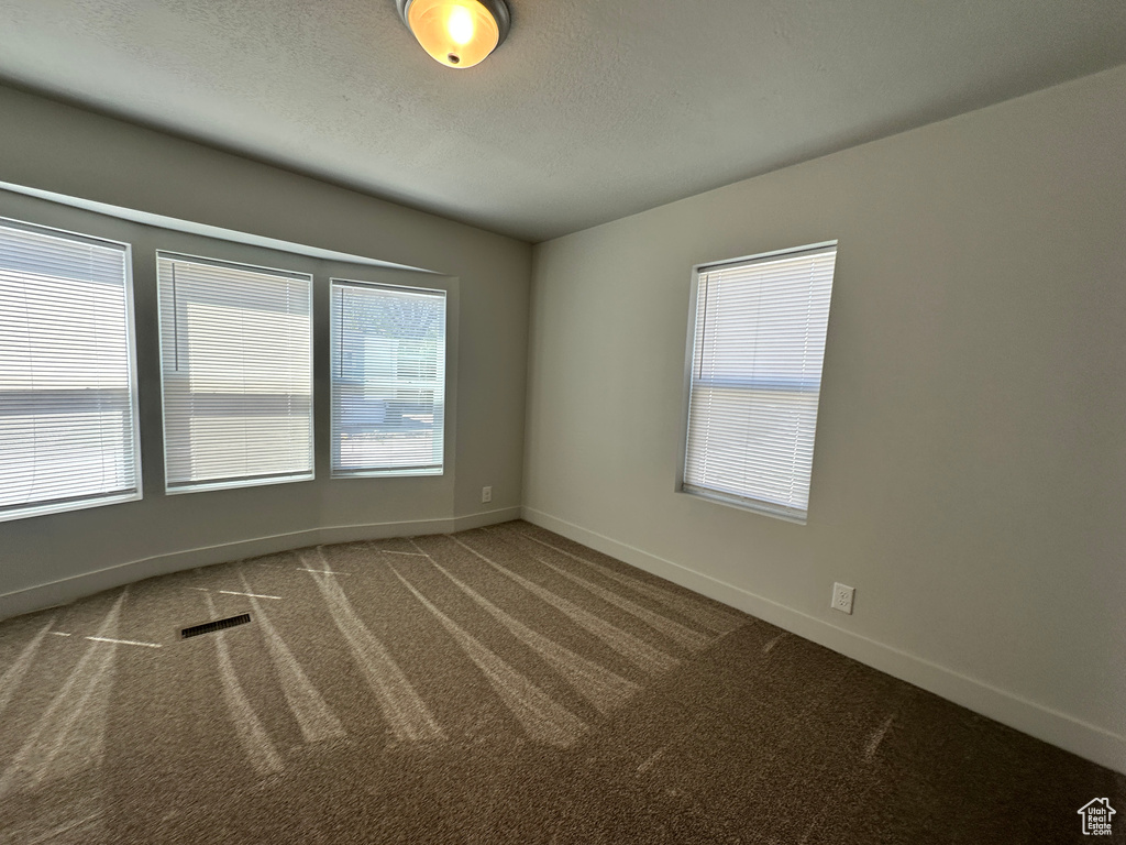 Unfurnished room featuring a textured ceiling, carpet, baseboards, and visible vents