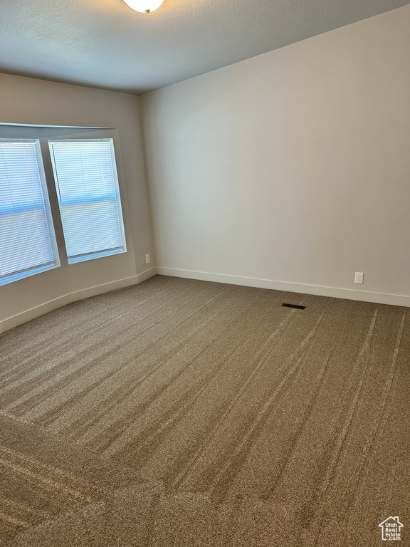Spare room featuring carpet flooring, visible vents, and baseboards