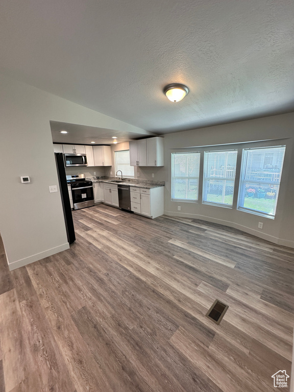 Kitchen with wood finished floors, white cabinetry, open floor plan, baseboards, and appliances with stainless steel finishes