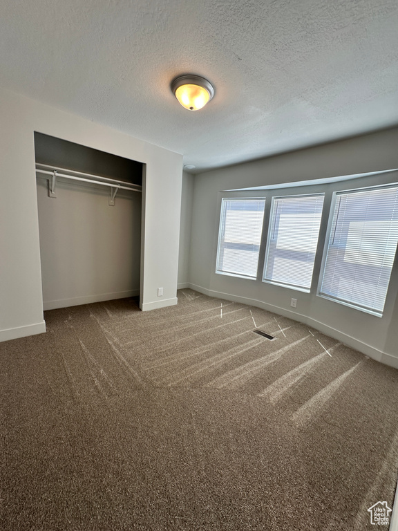 Unfurnished bedroom with carpet flooring, a closet, a textured ceiling, and baseboards