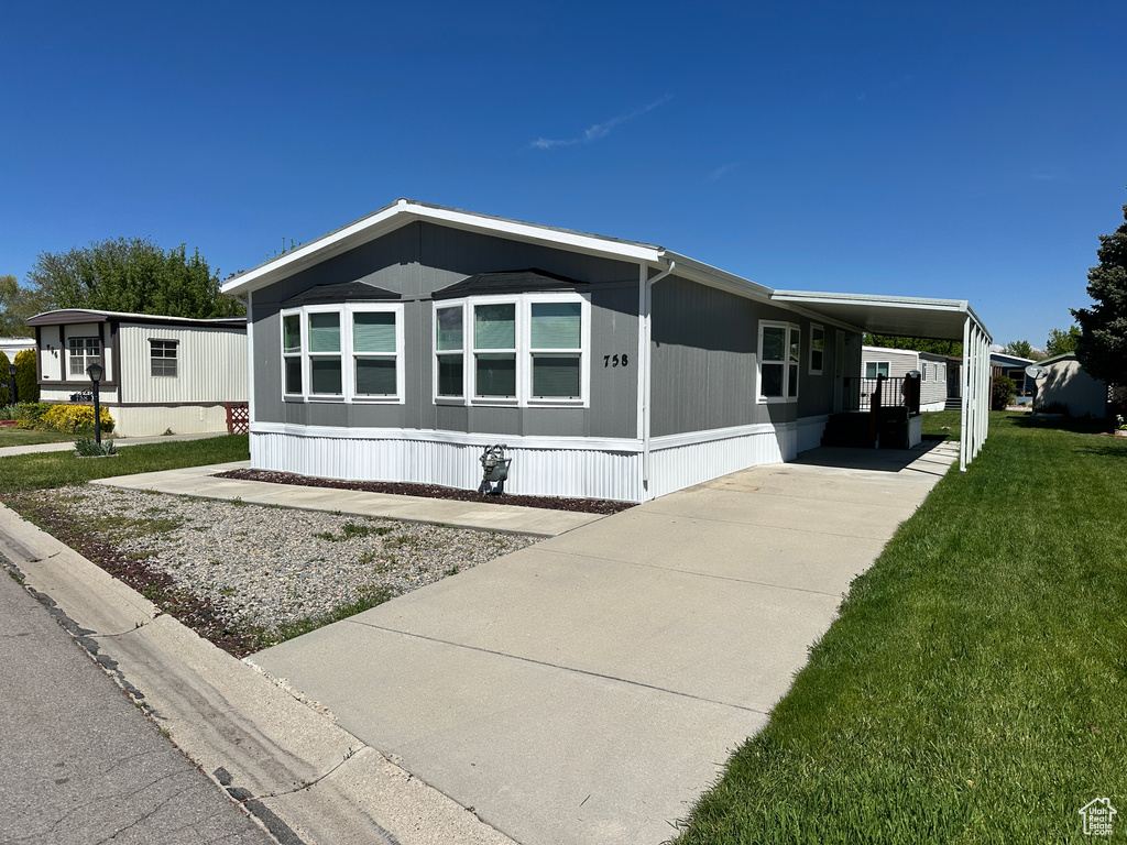 Manufactured / mobile home with concrete driveway, an attached carport, and a front lawn