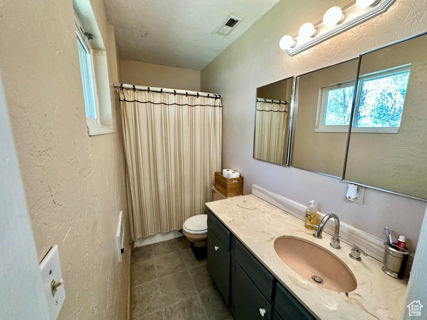 Bathroom with toilet, vanity, curtained shower, visible vents, and a textured wall