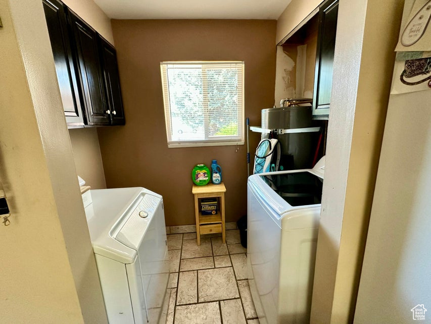 Laundry area featuring separate washer and dryer, cabinet space, stone tile flooring, and gas water heater