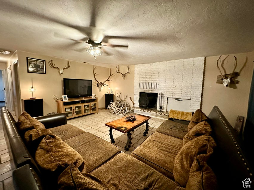 Living room with a textured ceiling, a brick fireplace, and ceiling fan