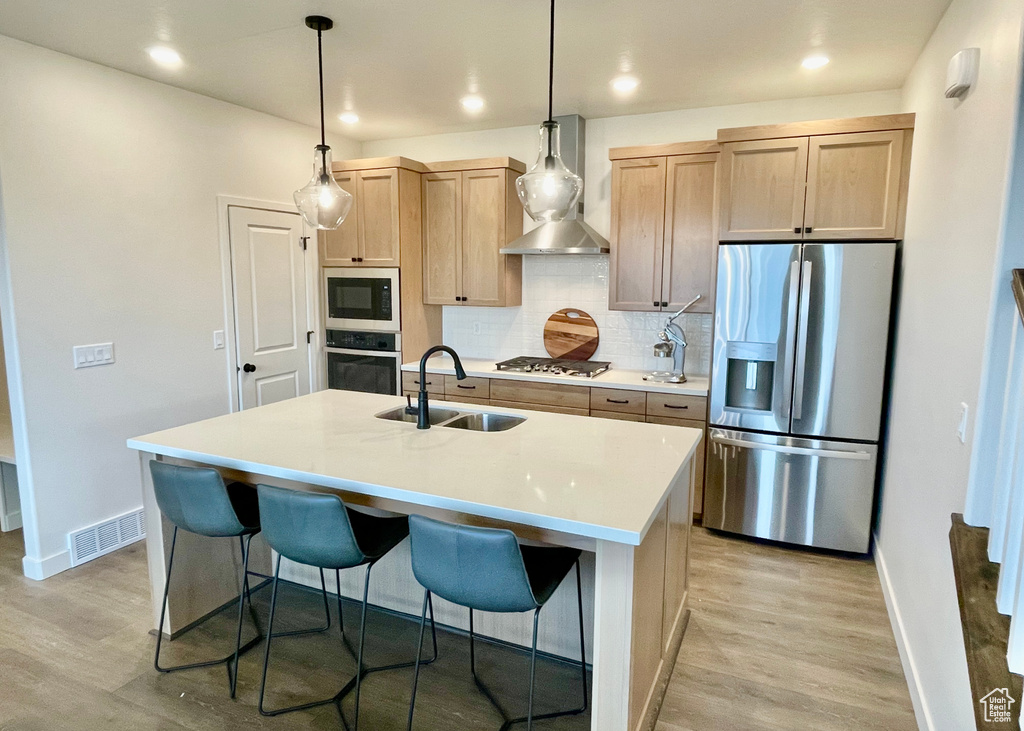 Kitchen with a sink, wall chimney exhaust hood, light wood-style flooring, baseboards, and appliances with stainless steel finishes