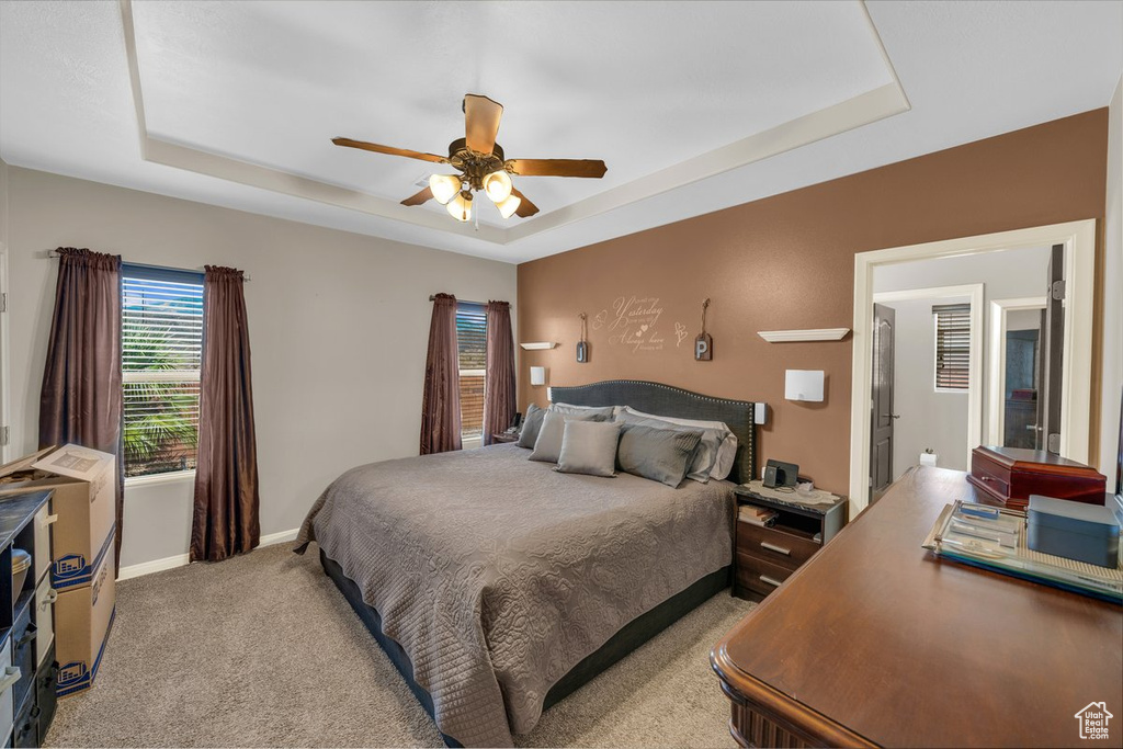 Bedroom with baseboards, a raised ceiling, light carpet, and ceiling fan