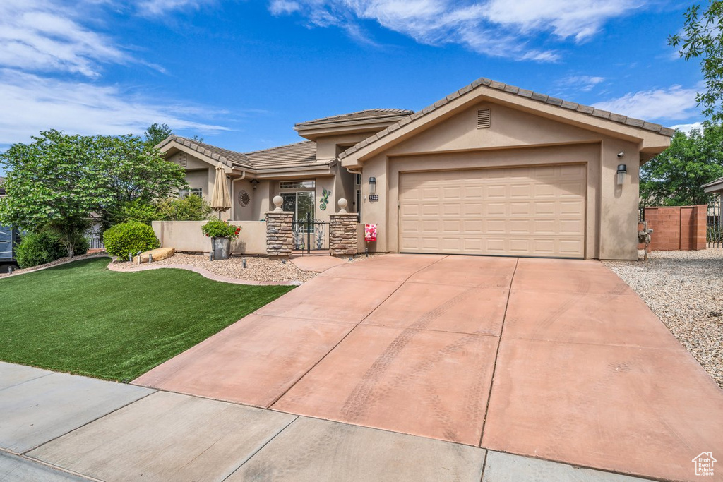 View of front facade with a garage, a tiled roof, stucco siding, concrete driveway, and a front lawn