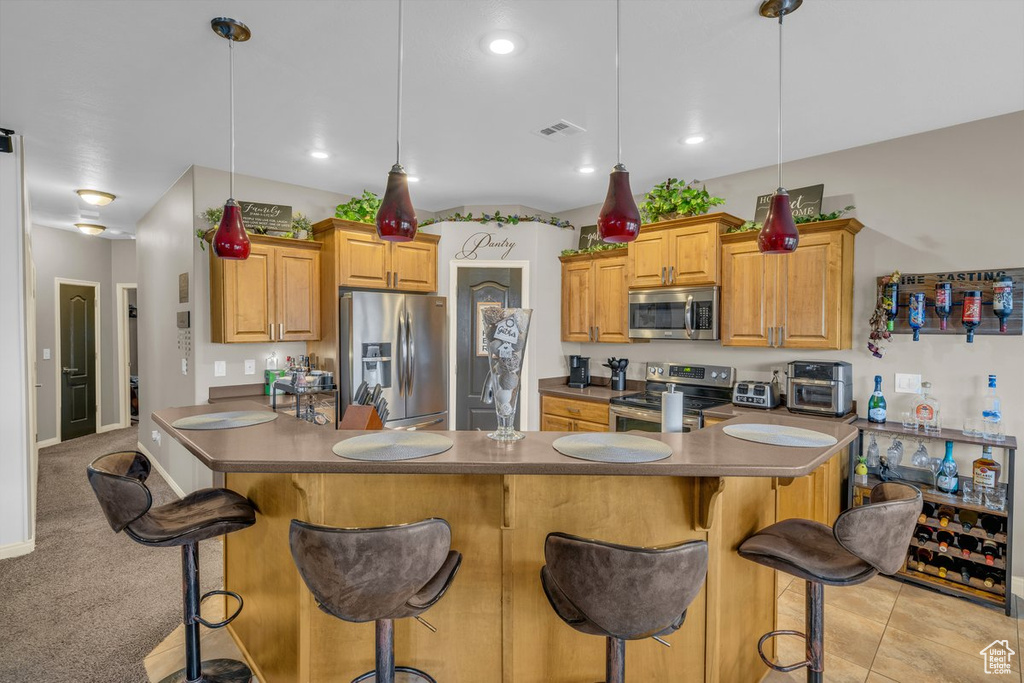 Kitchen with dark countertops, stainless steel appliances, visible vents, and a kitchen bar