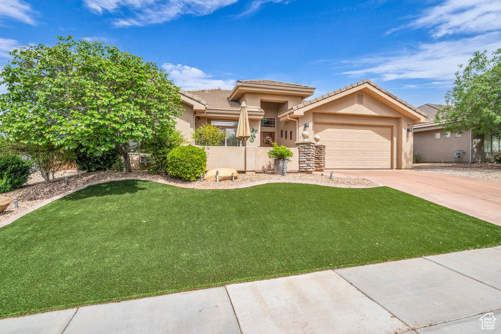 Prairie-style house featuring driveway, a tiled roof, an attached garage, stucco siding, and a front lawn
