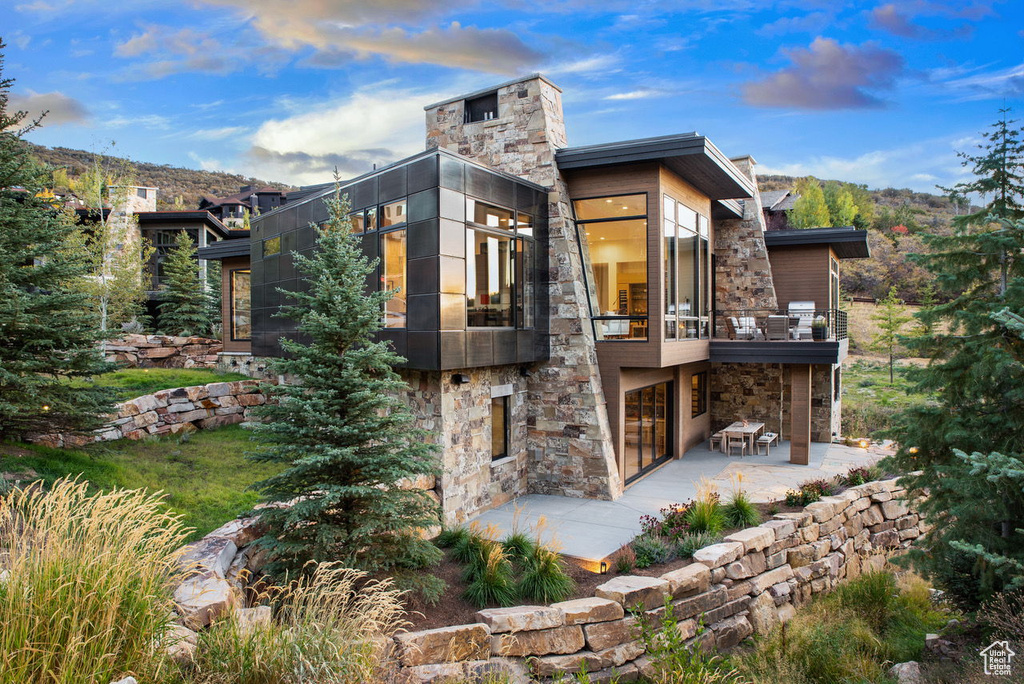 Rear view of property with stone siding, a patio, and a balcony