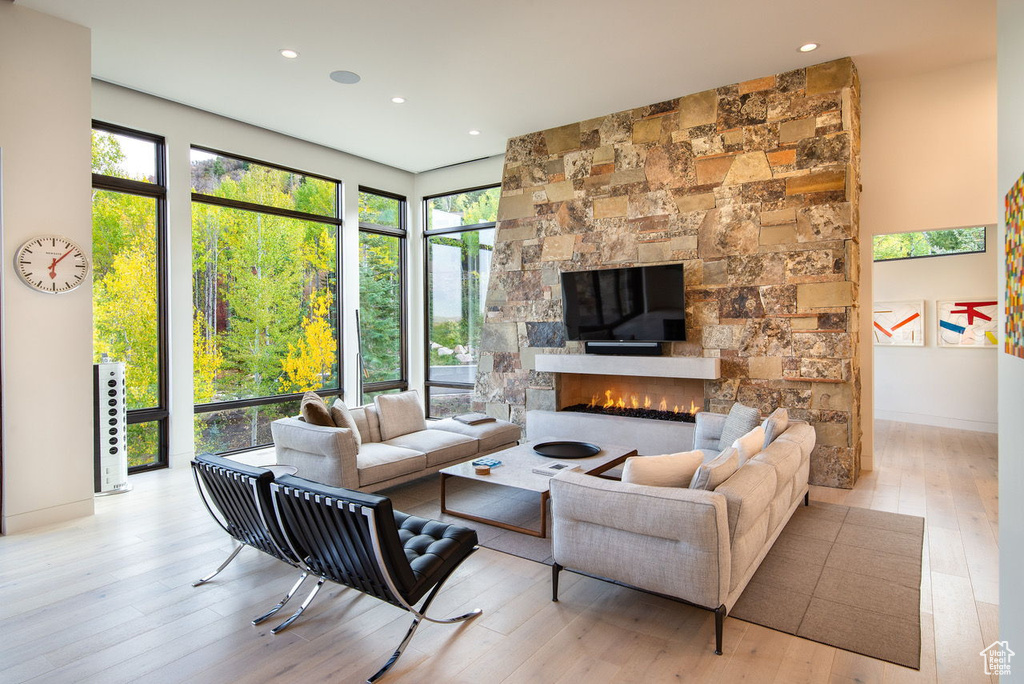 Living room with light wood-style flooring, a stone fireplace, and recessed lighting
