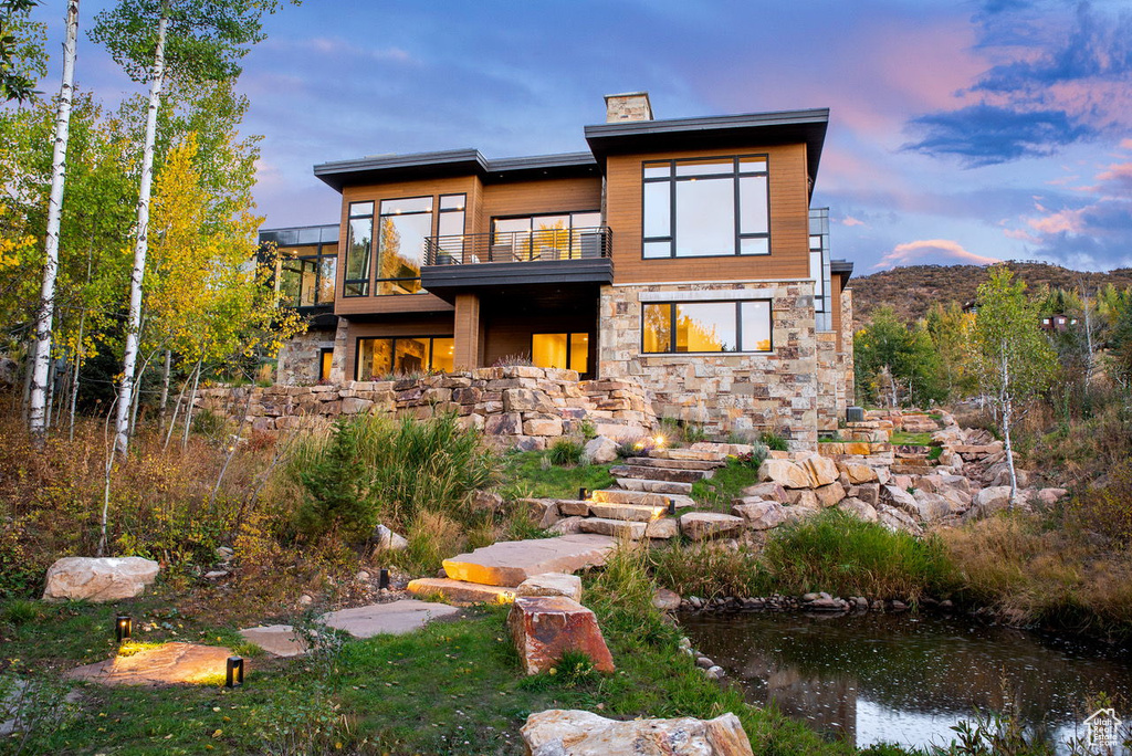 Rear view of property with a chimney, stone siding, and a balcony