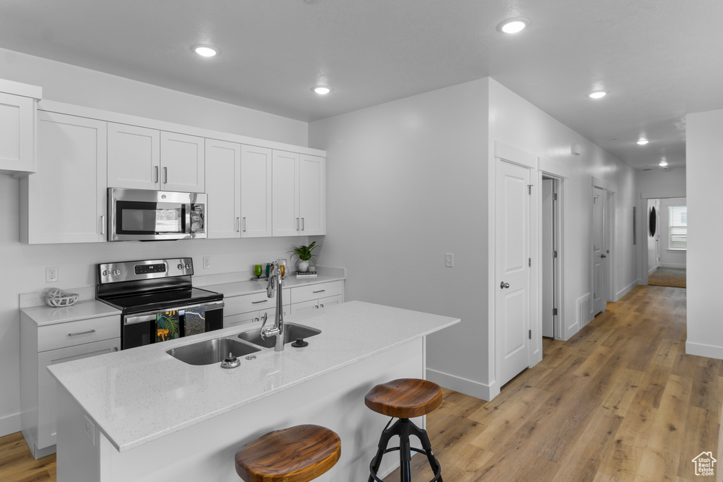 Kitchen featuring baseboards, a sink, a kitchen breakfast bar, light wood-style floors, and stainless steel appliances