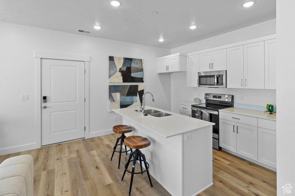 Kitchen featuring a sink, a breakfast bar, recessed lighting, light countertops, and appliances with stainless steel finishes