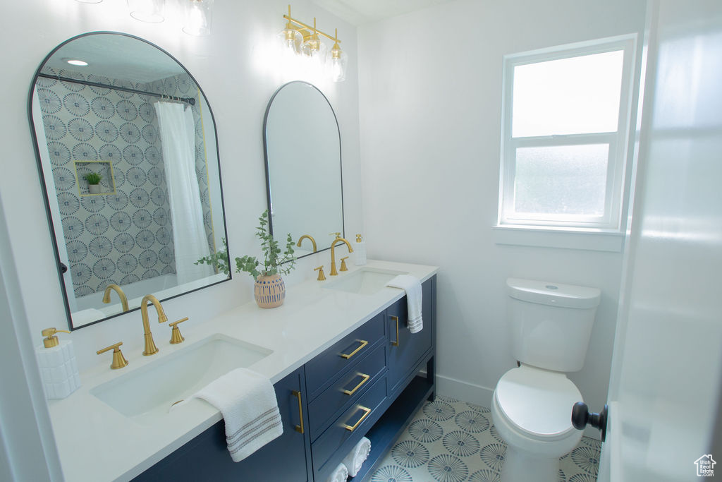 Bathroom featuring toilet, tile patterned floors, double vanity, and a shower with shower curtain