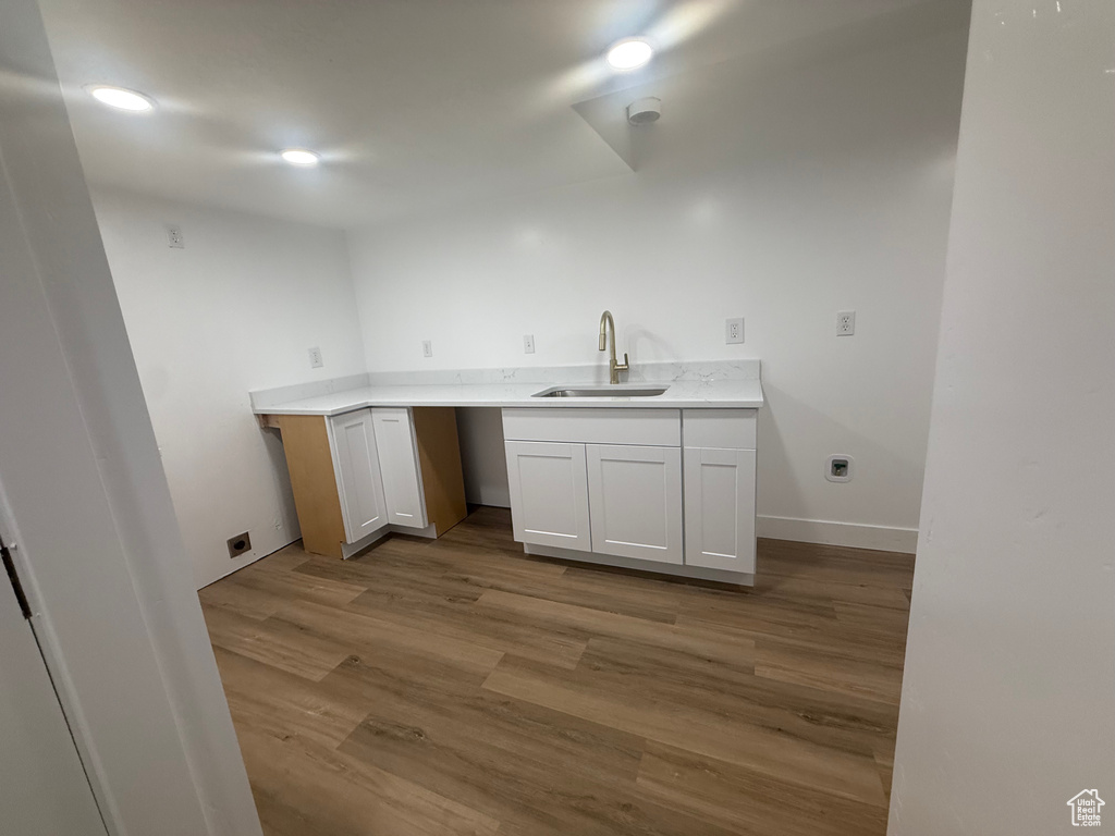 Kitchen with a sink, wood finished floors, light countertops, baseboards, and recessed lighting