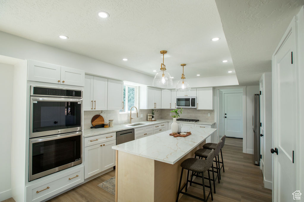 Kitchen featuring appliances with stainless steel finishes, wood finished floors, tasteful backsplash, a kitchen breakfast bar, and white cabinetry