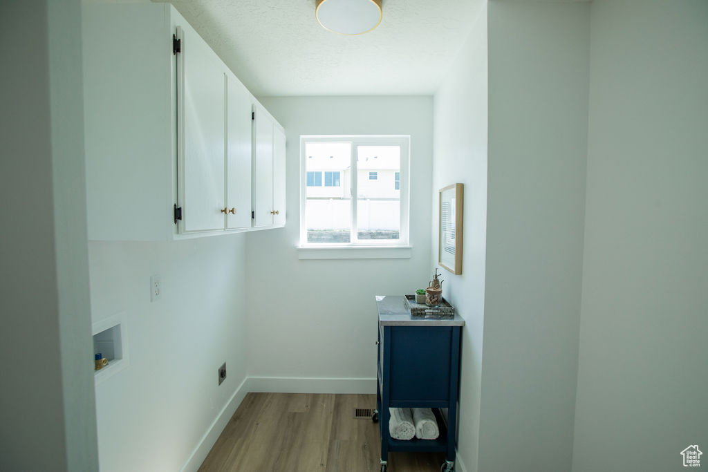 Laundry area with wood finished floors, cabinet space, hookup for a washing machine, baseboards, and a textured ceiling
