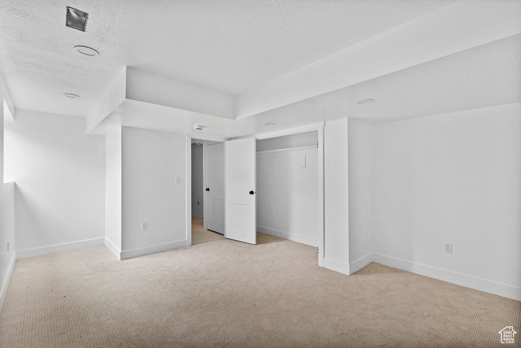 Unfurnished bedroom with light carpet, baseboards, a textured ceiling, and a closet