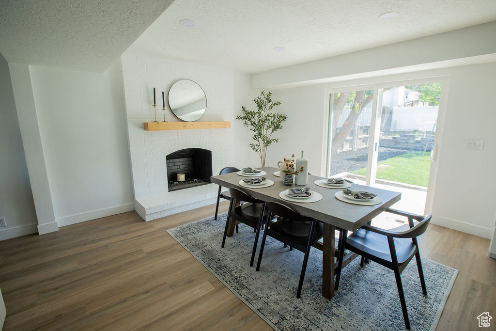 Dining area featuring a textured ceiling, baseboards, a brick fireplace, and wood finished floors
