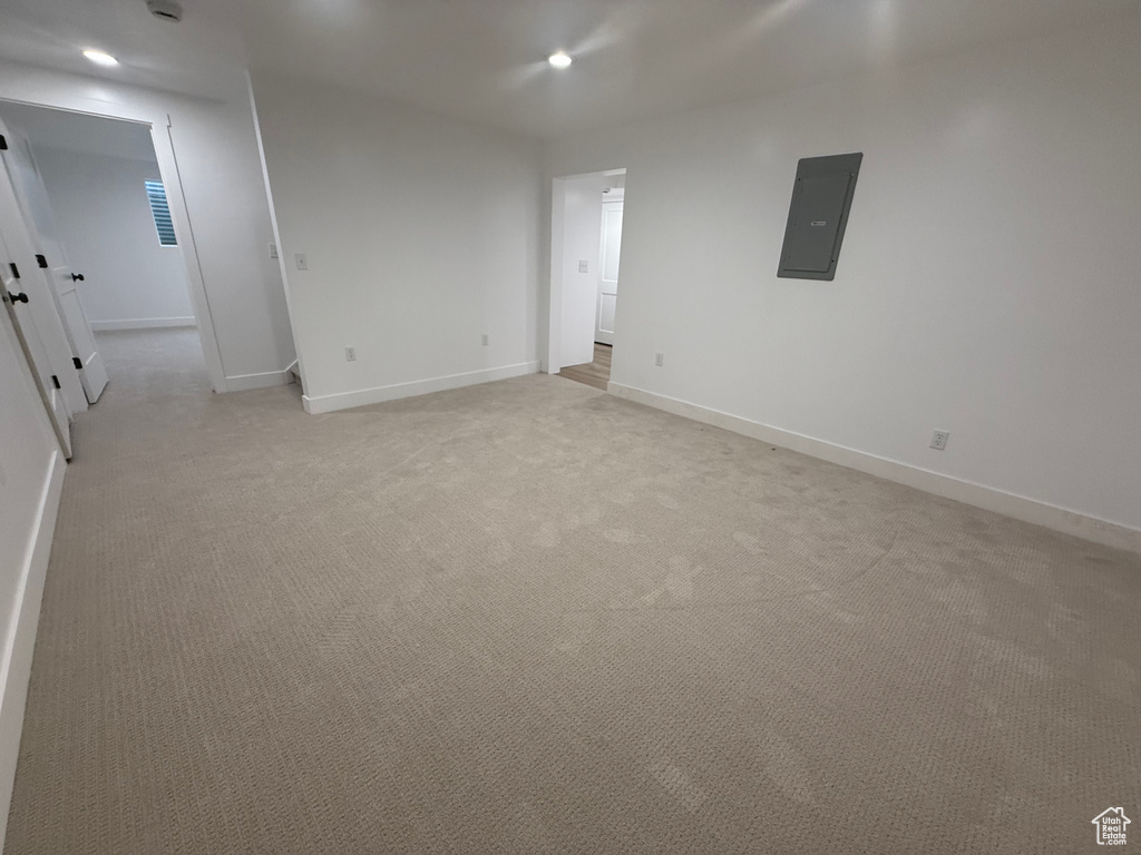 Empty room featuring electric panel, light colored carpet, baseboards, and recessed lighting